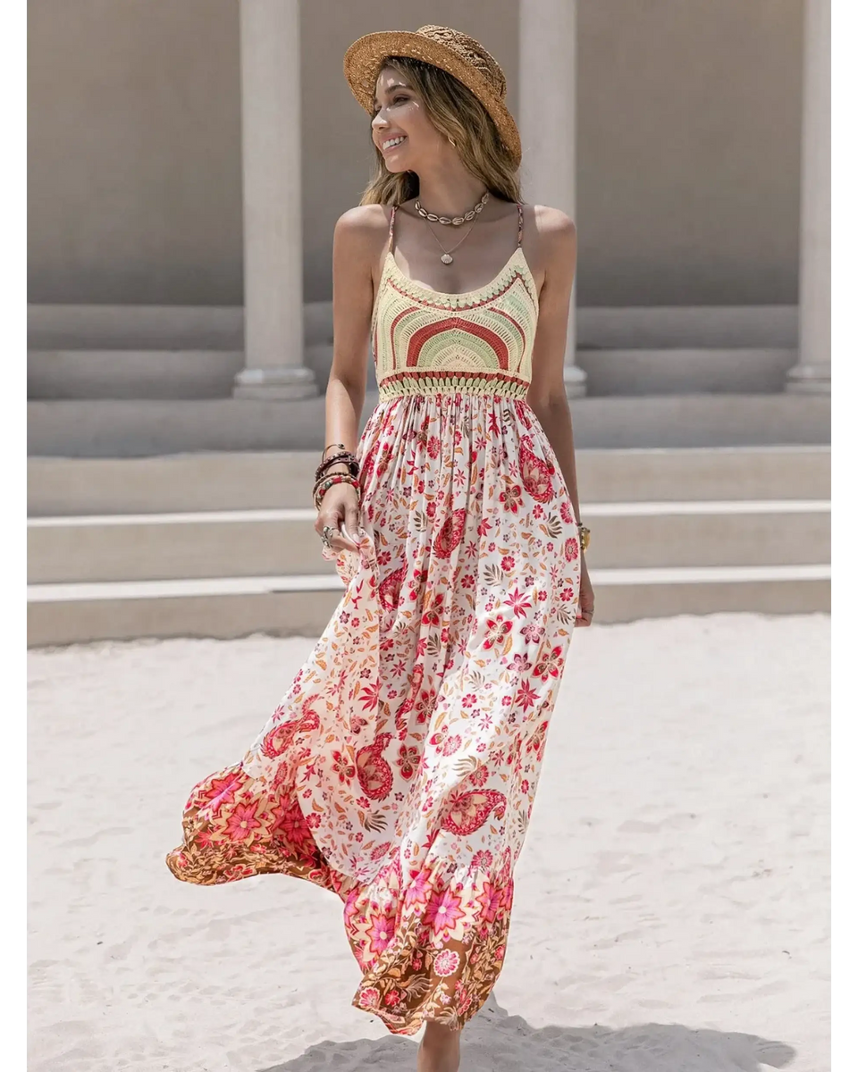 Woman wearing a crochet boho maxi dress with floral patterns and a straw hat on a sandy beach
