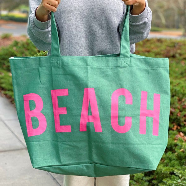 Green Canvas Beach Tote with pink BEACH lettering held by person outdoors