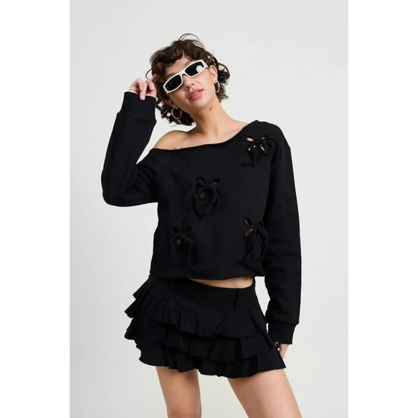 Emory Park off shoulder distressed top in black worn by model with ruffle mini skirt and white sunglasses