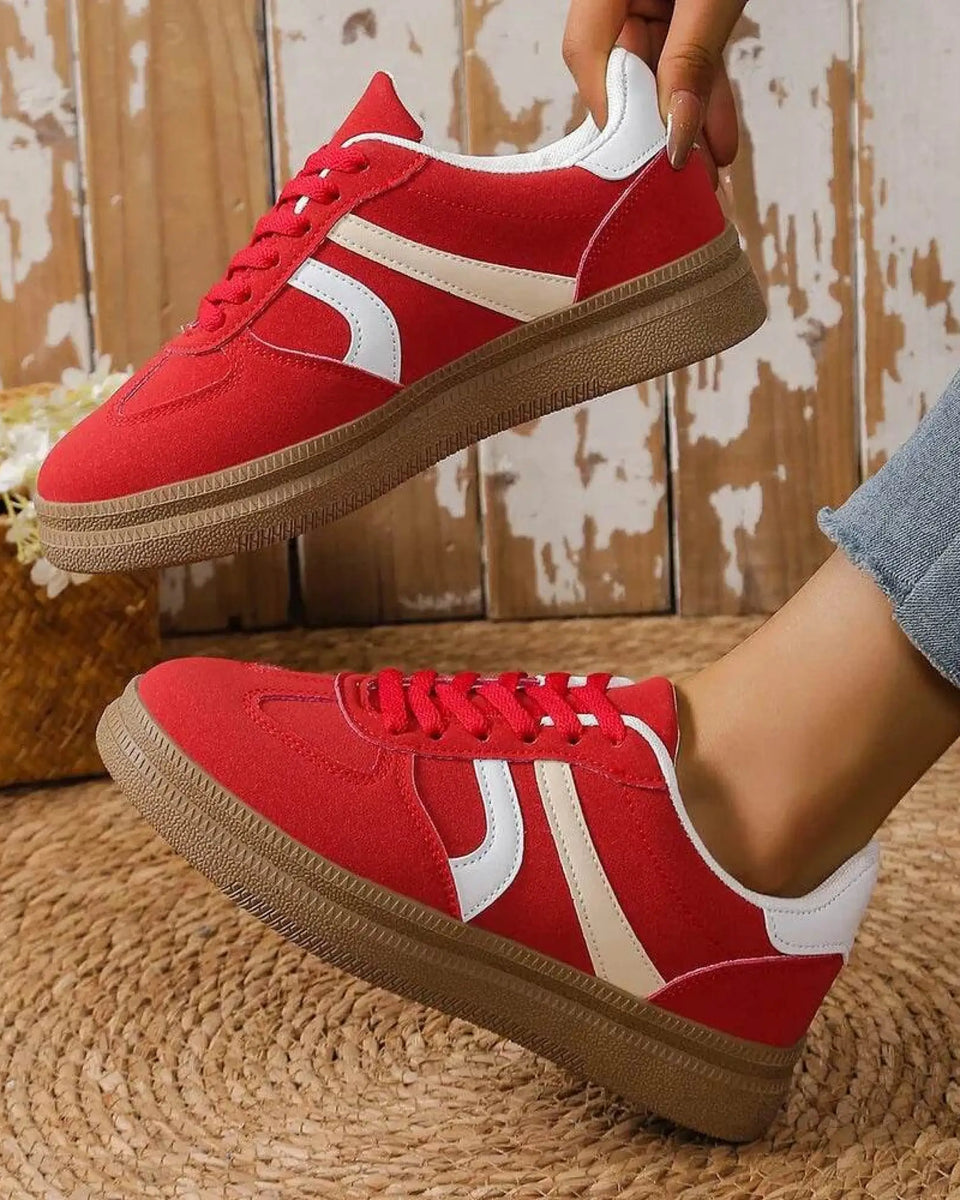 red contrast round toe sneakers with white stripes and brown sole worn with jeans