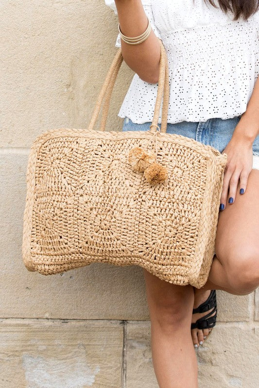 Babe Beachwaer Straw Summer Tote bag with woven design and pompom details held by woman in casual outfit
