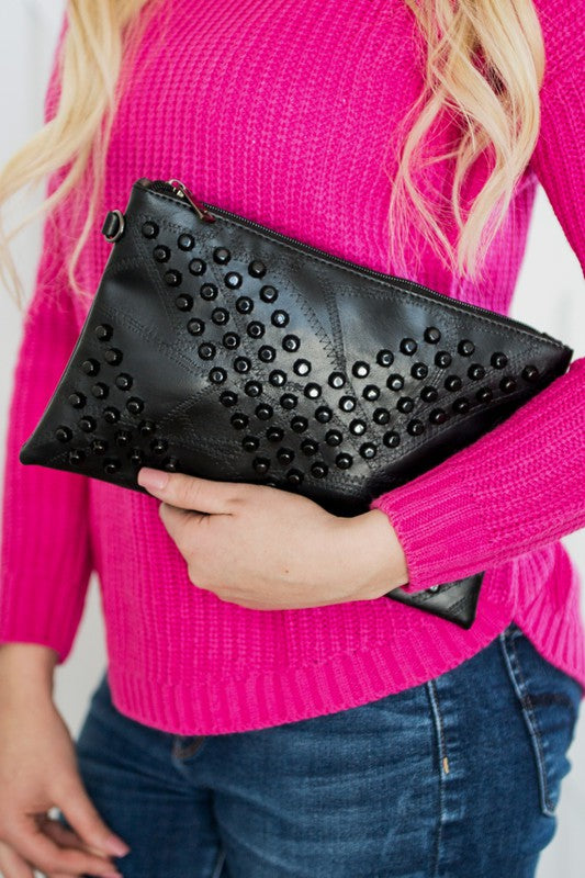 Black studded vacation evening clutch for women held by person in pink sweater and blue jeans