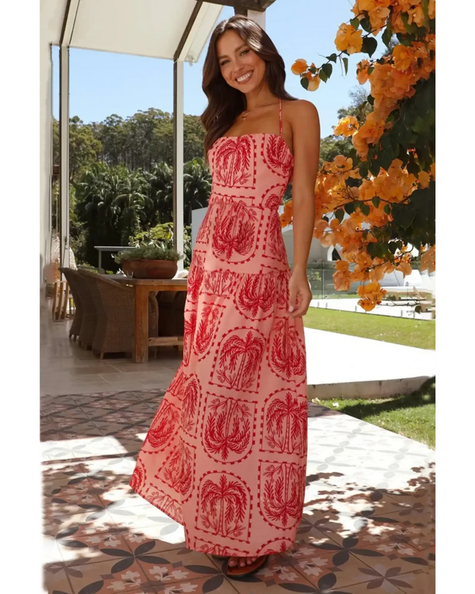 Coral empire waist maxi dress with red and pink tropical print worn by a smiling woman outdoors