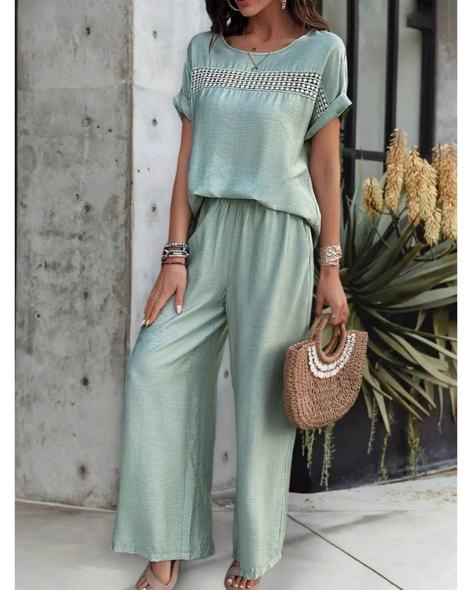 Light green satin pants set with short sleeve top and wide-leg pants accessorized with bracelets and a woven handbag