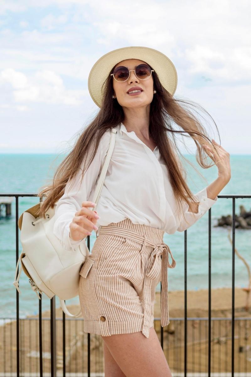 Woman wearing hat and sunglasses by the sea showcasing women's summer resort essentials outfit
