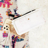 Babe Beachwear white cruise wristlet wallet for women placed on colorful rug with gold phone and makeup