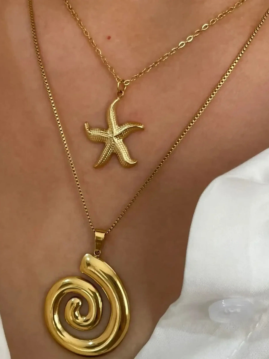 Elegant  18k gold starfish necklace worn with a spiral pendant layered on a person in a white shirt