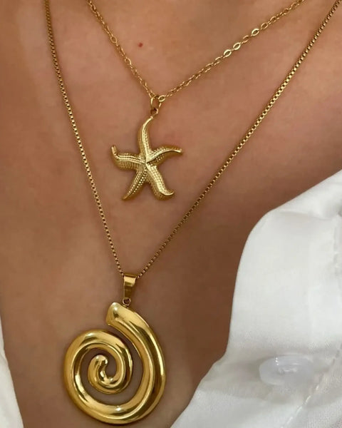Elegant  18k gold starfish necklace worn with a spiral pendant layered on a person in a white shirt