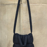 Black Babe Beachwear Jacie Puffer Mini Tote bag with long strap hanging on stone wall