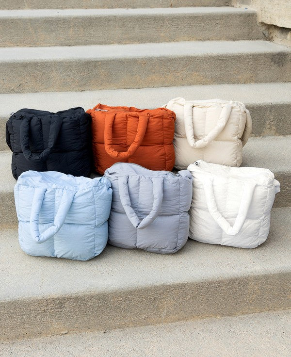 Babe Beachwear Jacie Puffer Mini Tote bags in black, orange, beige, light blue, gray, and white on concrete steps