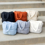 Babe Beachwear Jacie Puffer Mini Tote bags in black, orange, beige, light blue, gray, and white on concrete steps