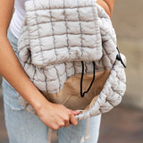 Babe Beachwear Puffer Backpack Lightweight in beige quilted design held by a woman in white top and jeans