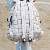 Babe Beachwaer Puffer Backpack Lightweight in light gray held by person wearing ripped jeans