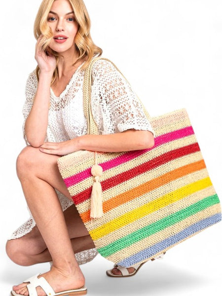 Woman holding large striped beach bag for women with colorful horizontal stripes and tassel detail