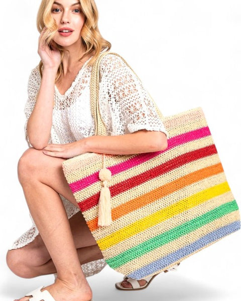 Woman holding large striped beach bag for women with colorful horizontal stripes and tassel detail