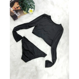 Beach Babes black long sleeve two piece swimsuit laid flat on white surface with magazine and plant