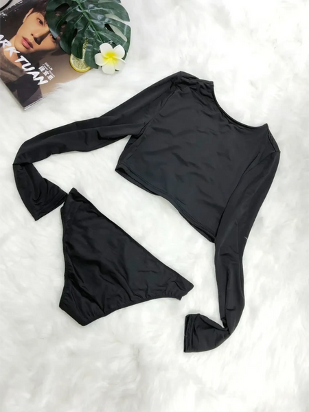 Beach Babes black long sleeve two piece swimsuit laid flat on white surface with magazine and plant
