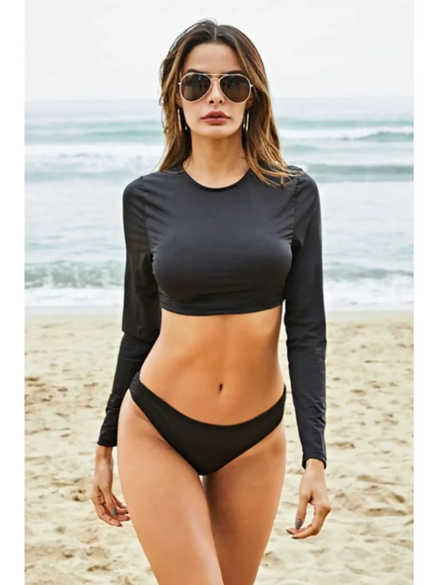 Beach Babes black long sleeve two piece swimsuit worn by model on sandy beach with ocean background