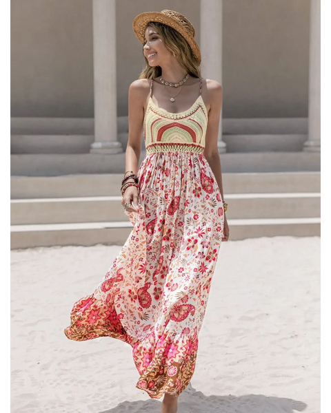 Woman wearing a crochet boho maxi dress with floral patterns and a straw hat on a sandy beach