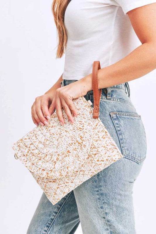 Babe Beachwaer boho ivory clutch bag with woven texture and brown wrist strap held by woman in white top and jeans