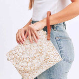 Babe Beachwaer boho ivory clutch bag with woven texture and brown wrist strap held by woman in white top and jeans