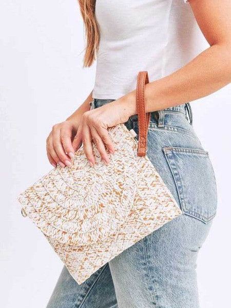 Babe Beachwaer boho ivory clutch bag with woven texture and brown wrist strap held by woman in white top and jeans
