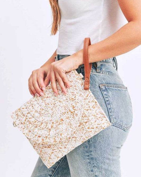 Babe Beachwaer boho ivory clutch bag with woven texture and brown wrist strap held by woman in white top and jeans
