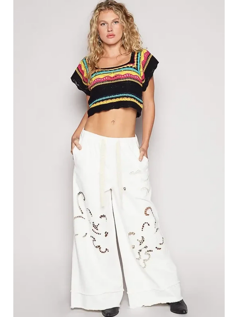 POL  boho knit beach top in multi-color worn with white wide-leg pants by a female model