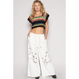 POL  boho knit beach top in multi-color worn with white wide-leg pants by a female model