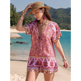 Babe Beachwear short sleeve romper with pink and red floral print worn by woman on beach