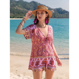 Babe Beachwear pink floral short sleeve romper worn by woman with straw hat on beach