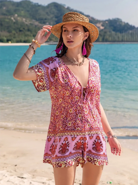 Babe Beachwear pink floral short sleeve romper worn by woman with straw hat on beach