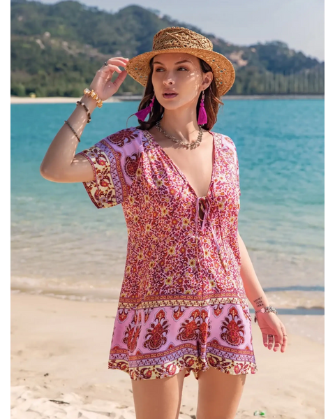 Babe Beachwear pink floral short sleeve romper worn by woman with straw hat on beach