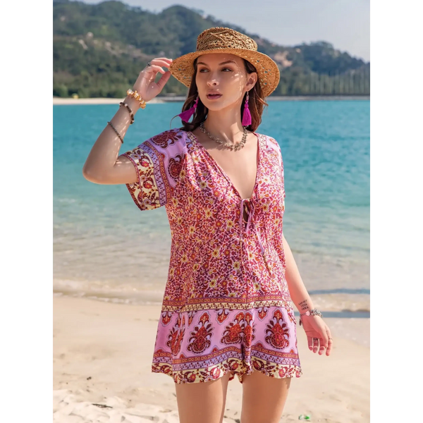 Babe Beachwear pink floral short sleeve romper worn by woman with straw hat on beach