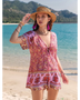 Babe Beachwear pink floral short sleeve romper worn by woman with straw hat on beach