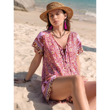 Woman wearing Babe Beachwear short sleeve romper with pink floral pattern and straw hat sitting on the beach