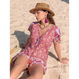Babe Beachwear floral short sleeve romper worn by woman sitting on sandy beach with straw hat
