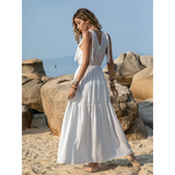 Babe Beachwear boho summer white crochet dress maxi style worn by a woman on a sandy beach with rocks