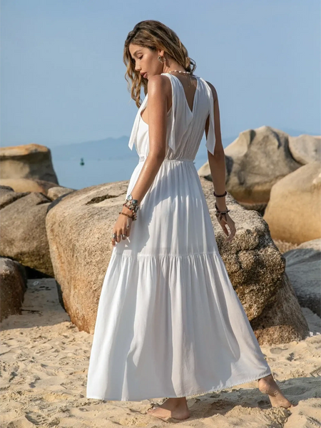 Babe Beachwear boho summer white crochet dress maxi style worn by a woman on a sandy beach with rocks