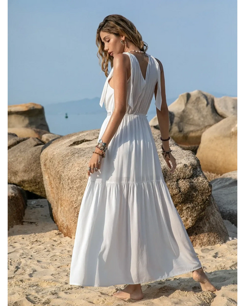 Babe Beachwear boho summer white crochet dress maxi style worn by a woman on a sandy beach with rocks
