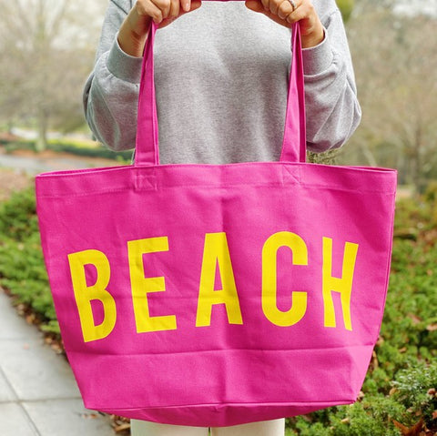 Bright pink Canvas Beach Tote bag with yellow BEACH text held by person outdoors