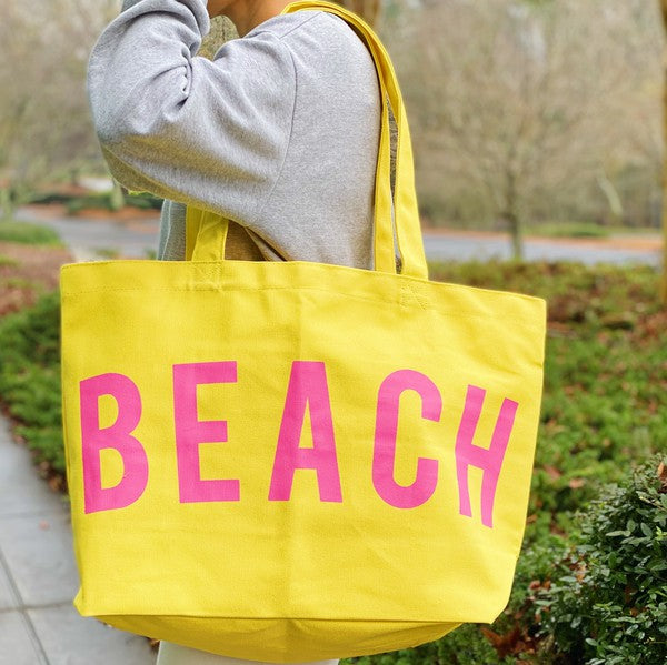 Babe Beachwear yellow Canvas Beach Tote with pink BEACH lettering carried on shoulder outdoors