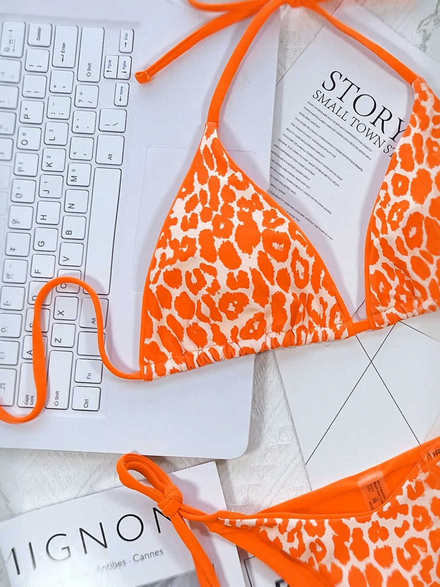 Beach Babes orange leopard print cheeky bottom triangle swimsuit laid on a laptop keyboard on marble surface