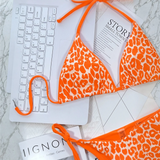 Beach Babes orange leopard print cheeky bottom triangle swimsuit laid on a laptop keyboard on marble surface