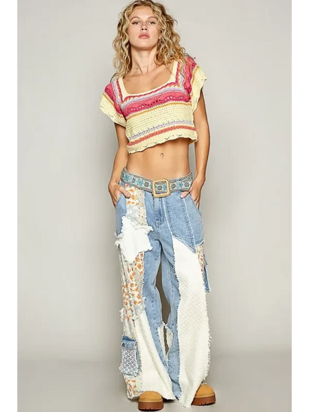 Model wearing a chic crochet crop top for beach in pink and yellow paired with patchwork jeans