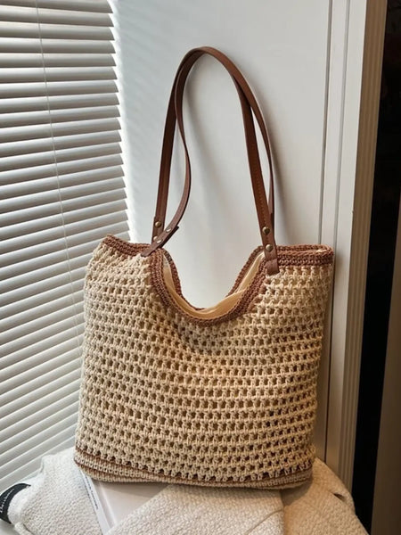 crochet tote bag with leather handles in beige with brown trim shown hanging against a window