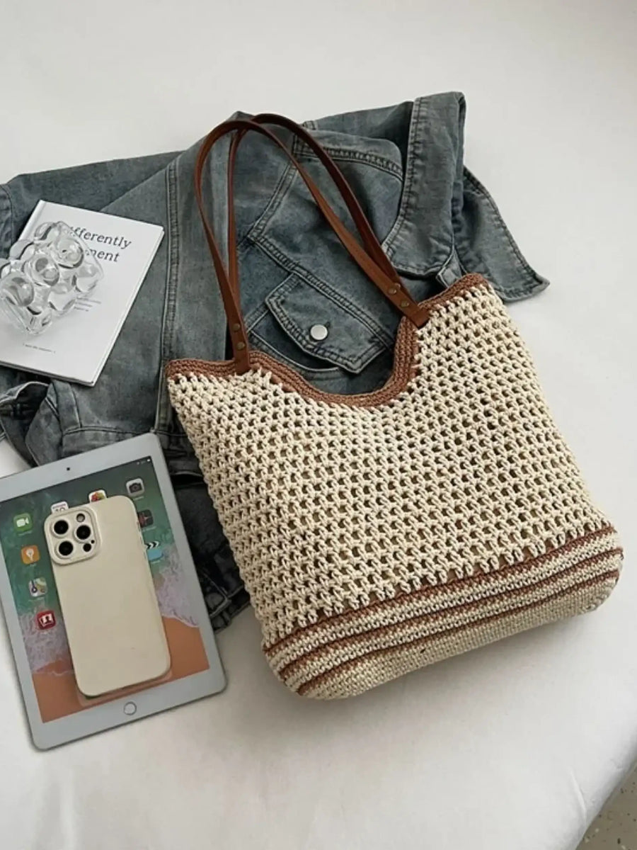 crochet tote bag with leather handles in beige and brown placed on a bed with a denim jacket, tablet, and phone