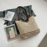 crochet tote bag with leather handles in beige and brown placed on a bed with a denim jacket, tablet, and phone