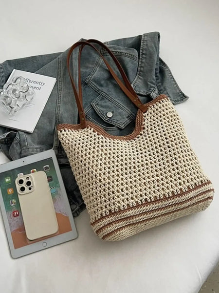 crochet tote bag with leather handles in beige and brown placed on a bed with a denim jacket, tablet, and phone