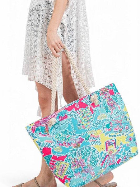 Babe Beachwear easy to pack summer beach bag with colorful tropical print carried by woman in white dress